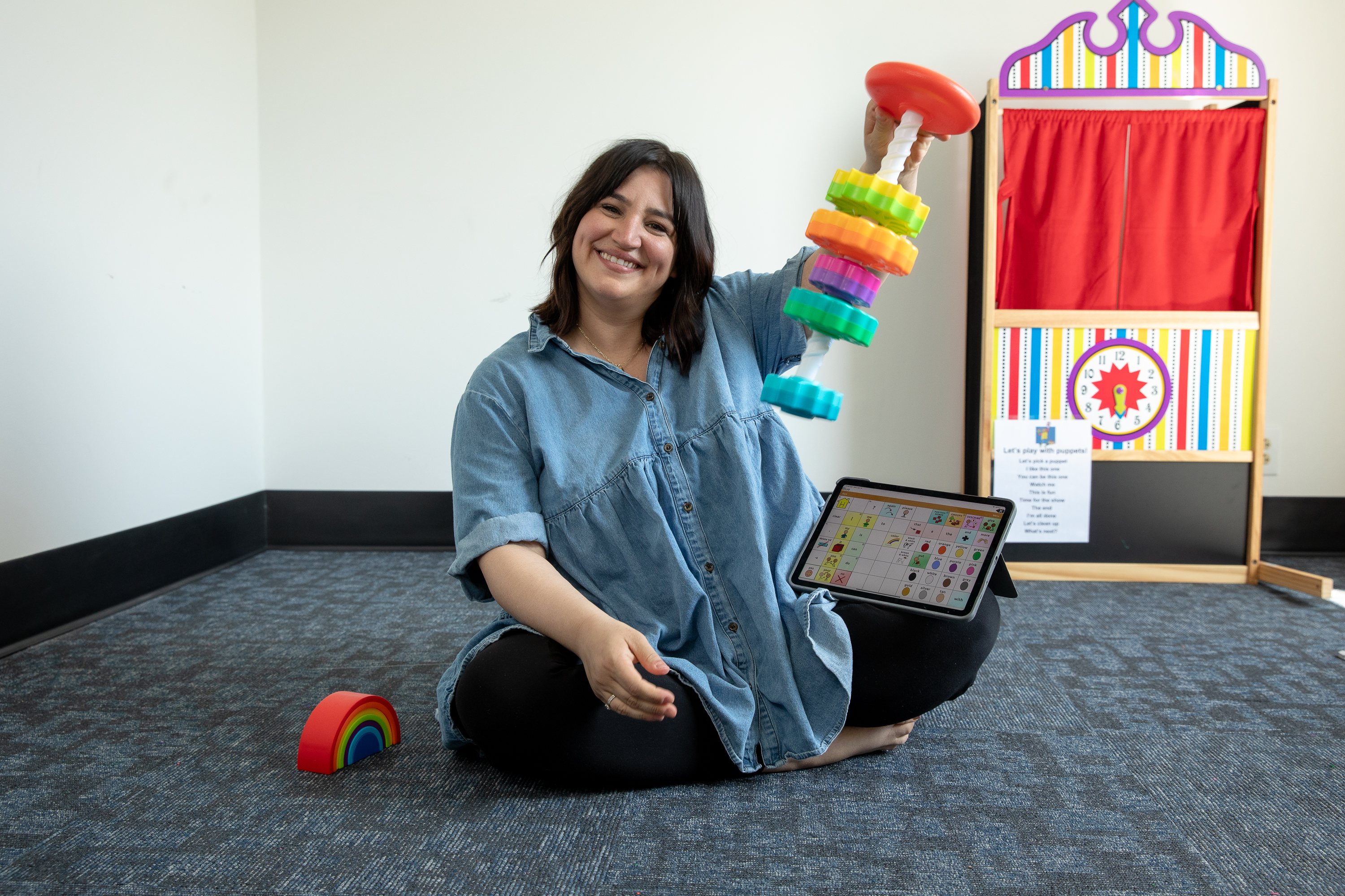 Nicole sitting on the floor holding a colorful stacking toy, with therapy tools around her