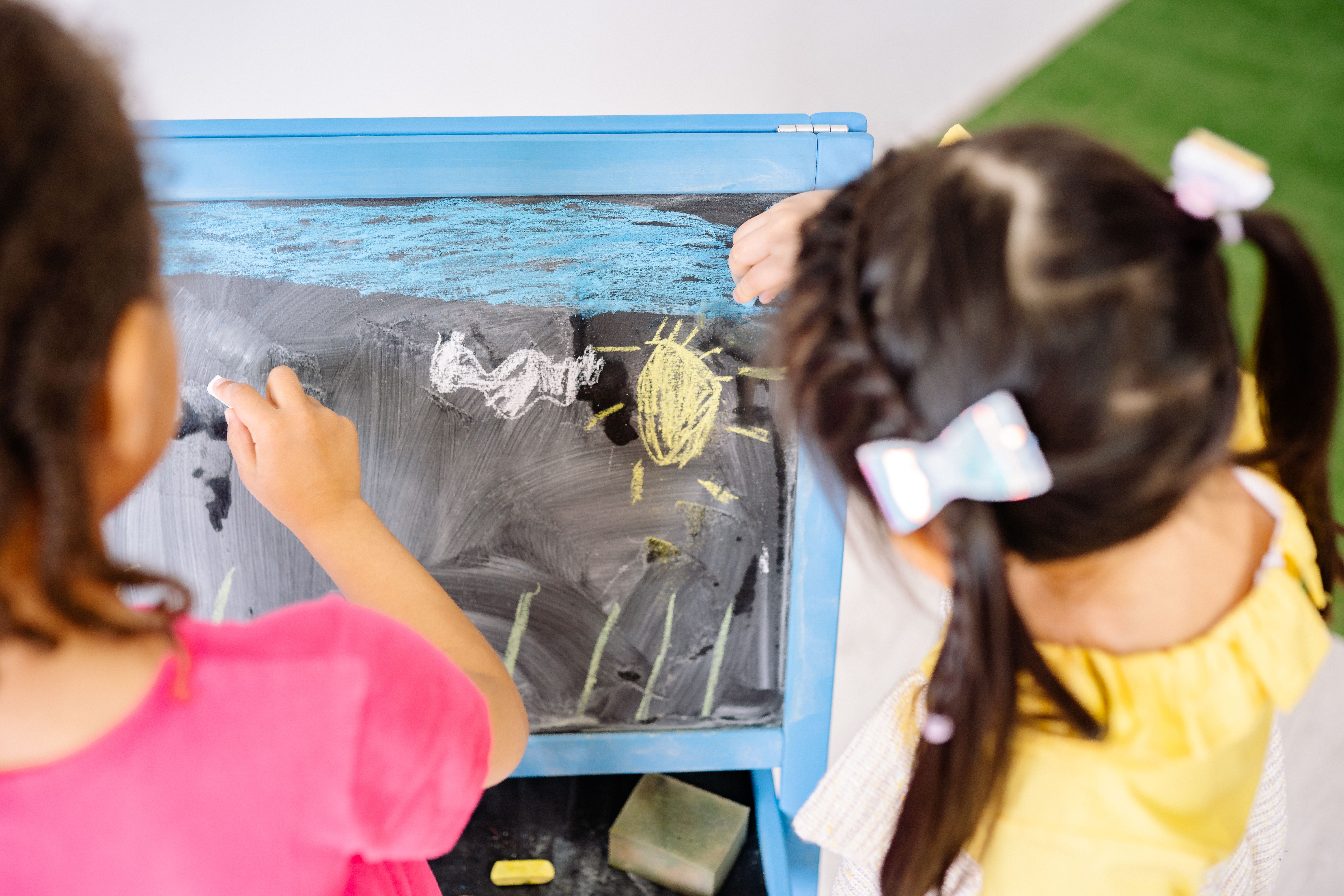 Two children drawing together at a chalkboard easel